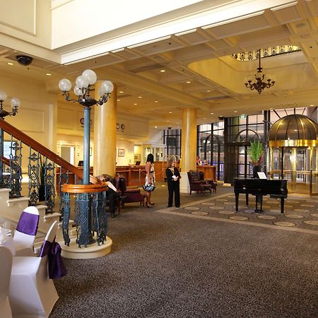 Stamford Grand Adelaide Hotel Glenelg Interiør billede The photo shows a luxurious interior of a hotel or a restaurant lobby. There is an elegant staircase with ornate railings leading to an upper level. The space features high ceilings with decorative chandeliers and ample natural light coming through l