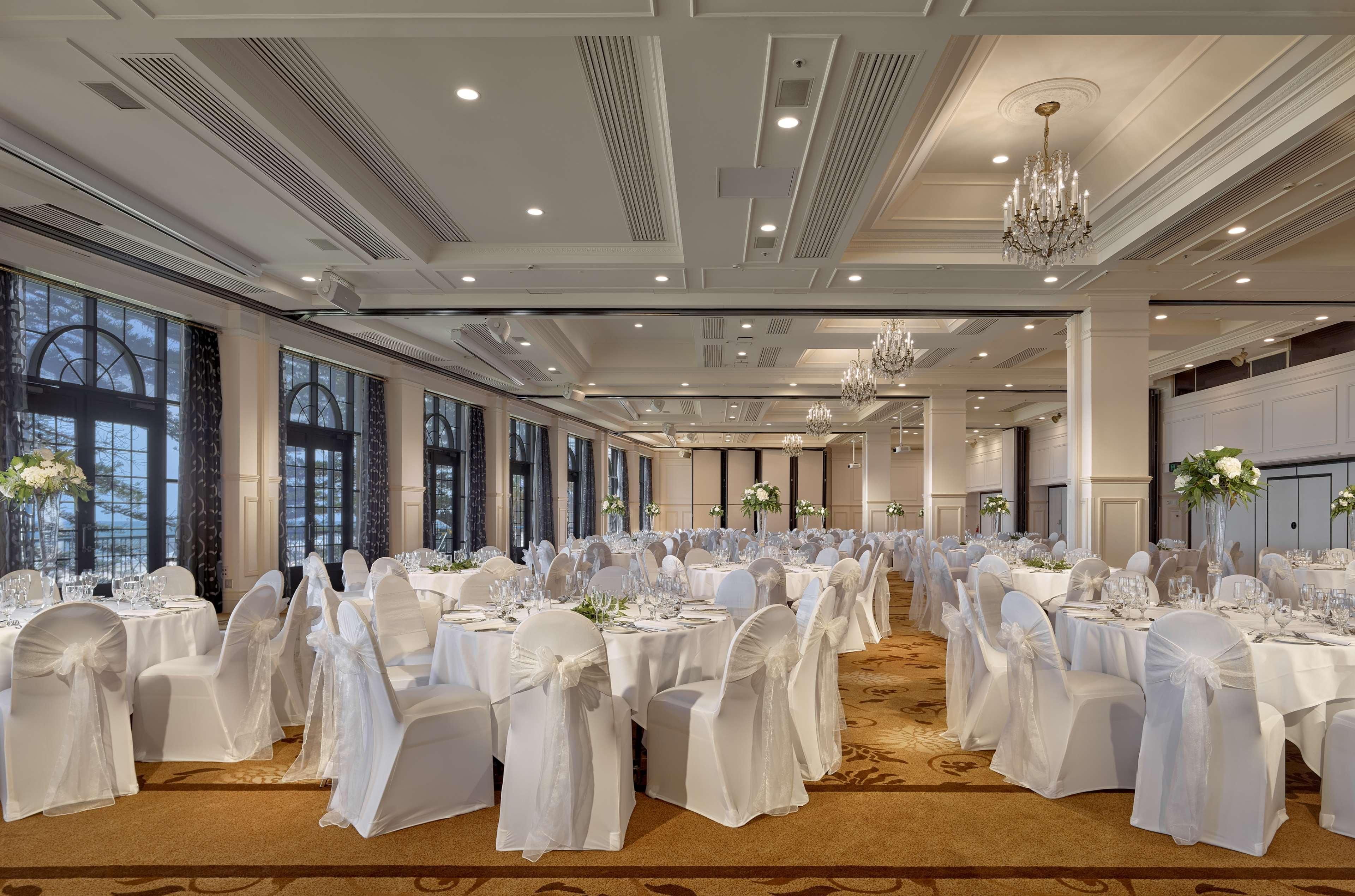 Stamford Grand Adelaide Hotel Glenelg Eksteriør billede The photo depicts an elegantly arranged banquet hall or dining area. The space features multiple round tables, each set with white tablecloths and decorated with floral centerpieces. The chairs are covered in white fabric, contributing to a formal at