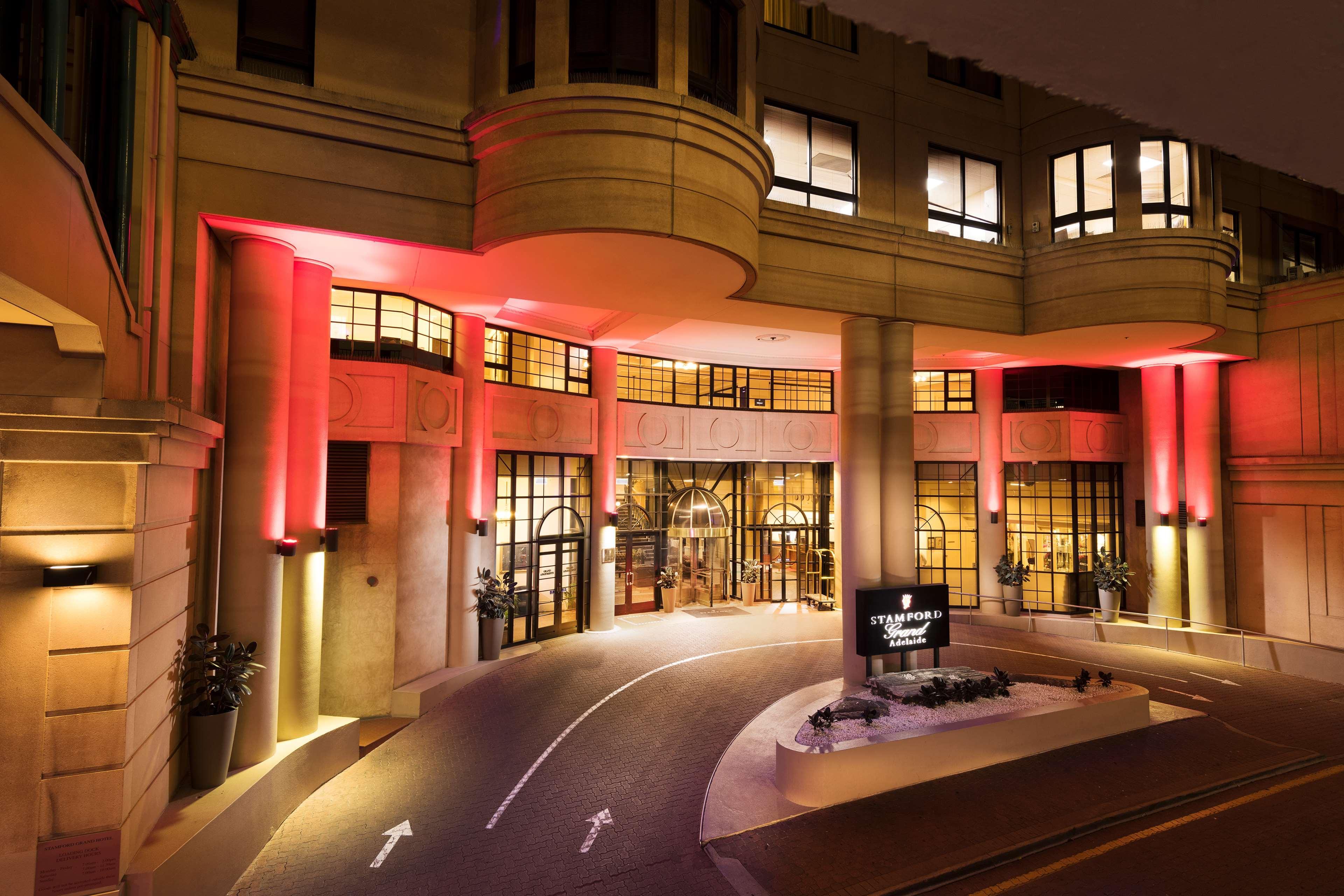 Stamford Grand Adelaide Hotel Glenelg Eksteriør billede The photo shows the entrance of a hotel or luxury building at night. The façade features a modern architectural style with large windows and an elegant entrance. The area is illuminated with red lighting, creating an inviting atmosphere. There appear