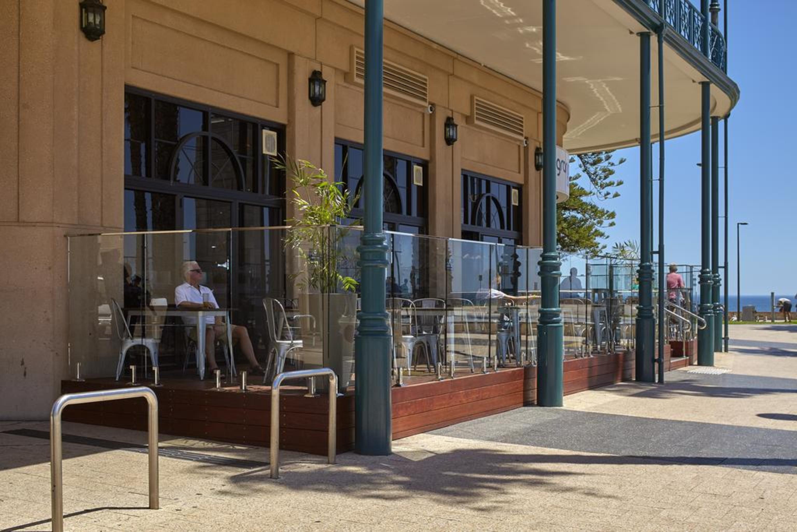 Stamford Grand Adelaide Hotel Glenelg Eksteriør billede The photo shows the exterior of a cafe or restaurant with a large outdoor seating area. There are glass barriers around the seating, providing a view of the outside while maintaining a sense of enclosure. The building has a modern architectural style