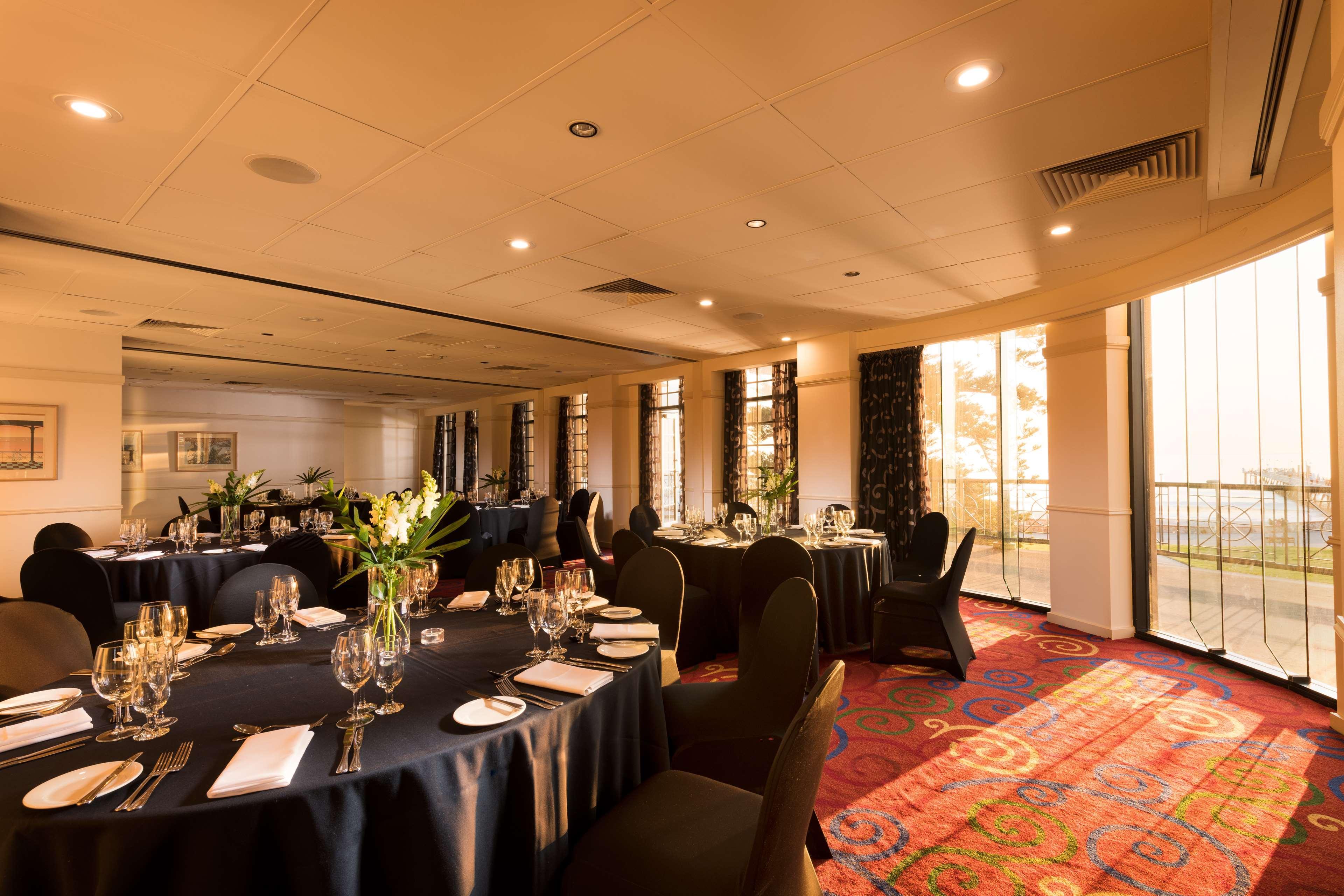 Stamford Grand Adelaide Hotel Glenelg Eksteriør billede The photo shows a well-decorated event space or dining area. There are several round tables draped in dark tablecloths, each set with elegant dinnerware, including glasses and cutlery. The room features large windows that allow natural light to flood