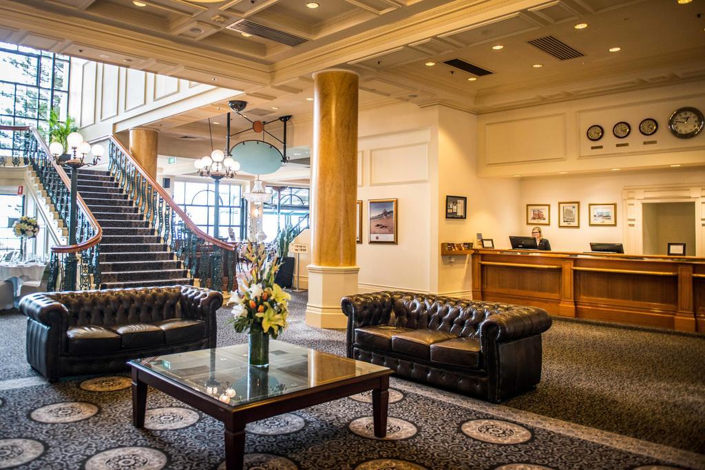 Stamford Grand Adelaide Hotel Glenelg Eksteriør billede The photo depicts a hotel lobby featuring a spacious and elegant design. There are two dark leather sofas arranged in front of a glass coffee table, adorned with a floral centerpiece. The lobby has a refined atmosphere, highlighted by large windows t